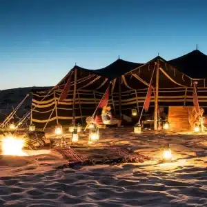 Panoramic scene of Oman tours showing desert dunes, wadis, mountains, coastline, camels, and traditional Omani architecture at sunset