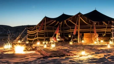 Panoramic scene of Oman tours showing desert dunes, wadis, mountains, coastline, camels, and traditional Omani architecture at sunset