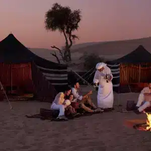 Panoramic scene of Oman tours showing desert dunes, wadis, mountains, coastline, camels, and traditional Omani architecture at sunset