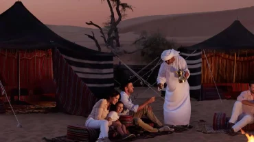 Panoramic scene of Oman tours showing desert dunes, wadis, mountains, coastline, camels, and traditional Omani architecture at sunset