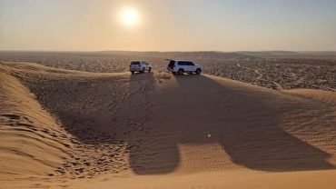 Panoramic scene of Oman tours showing desert dunes, wadis, mountains, coastline, camels, and traditional Omani architecture at sunset